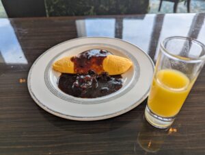 濃厚なデミグラスソースがかけられた焼きたてオムレツとフレッシュオレンジジュース