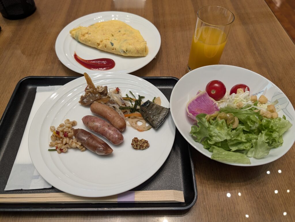 プレーンオムレツ、ソーセージ、サラダ、オレンジジュースが並ぶ朝食セット