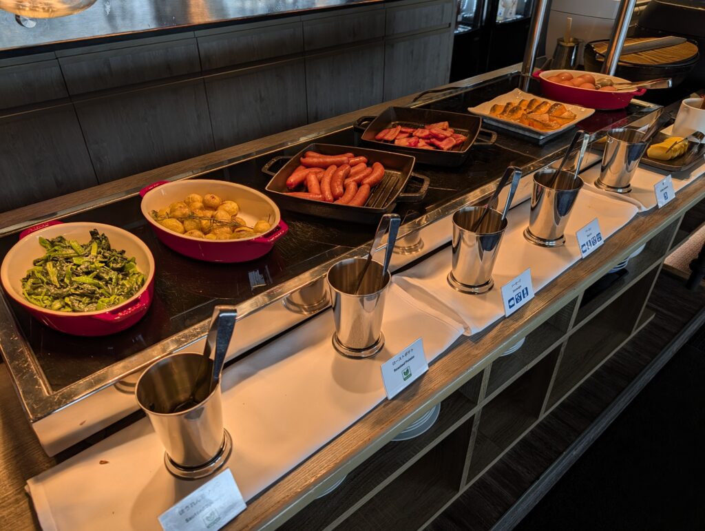 ソーセージやベーコン、温野菜などがカラフルな鍋に並ぶホットミールコーナー